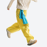 
                  
                    Unisex quick-dry water-repellent hiking pants - yellow wide-leg hiking pants with blue waist cloth, stride side walking view
                  
                